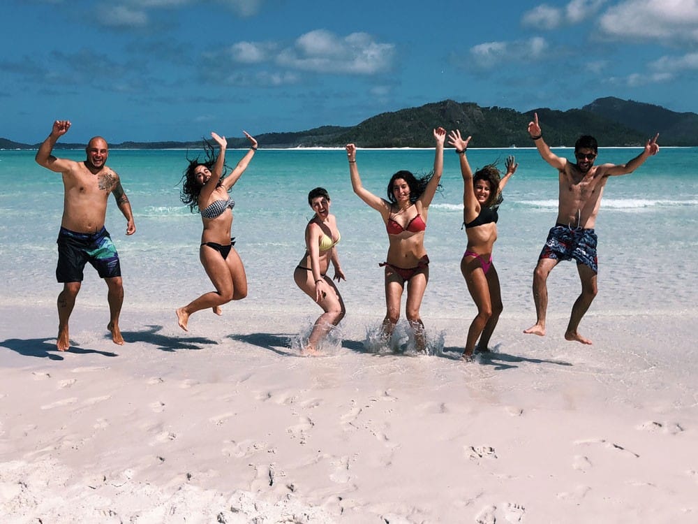 Experiencia en Australia grupo de 6 jóvenes en bañador saltando en la orilla de una playa